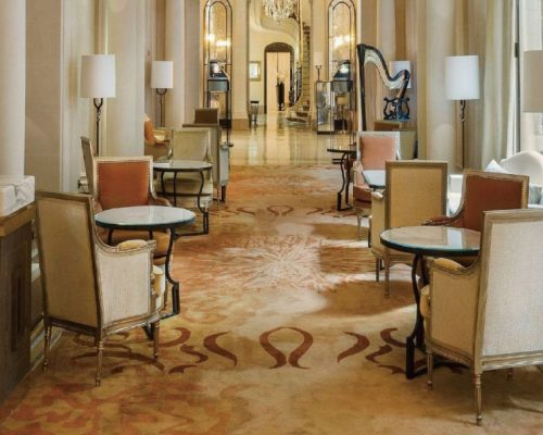 A hotel lobby with chairs and tables on a hand tufted carpet